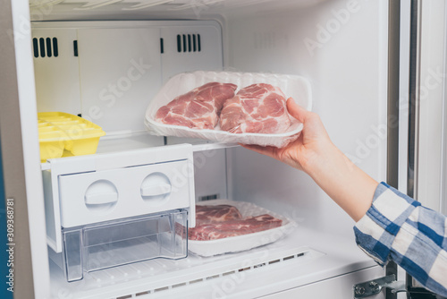 cropped view of woman taking out frozen meat from freezer photo