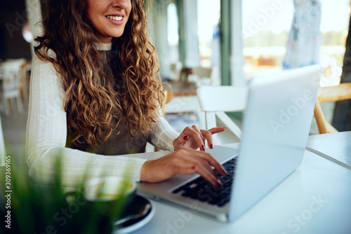 Attractive young curly brunette enjoying her tea/coffee and working on laptop