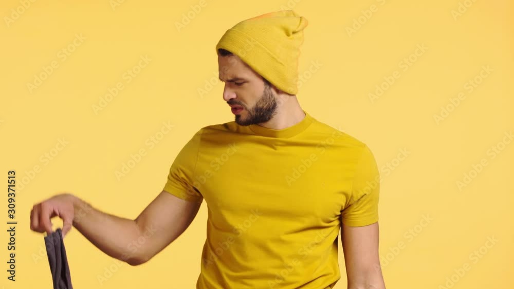 dissatisfied man smelling stinky socks isolated on yellow