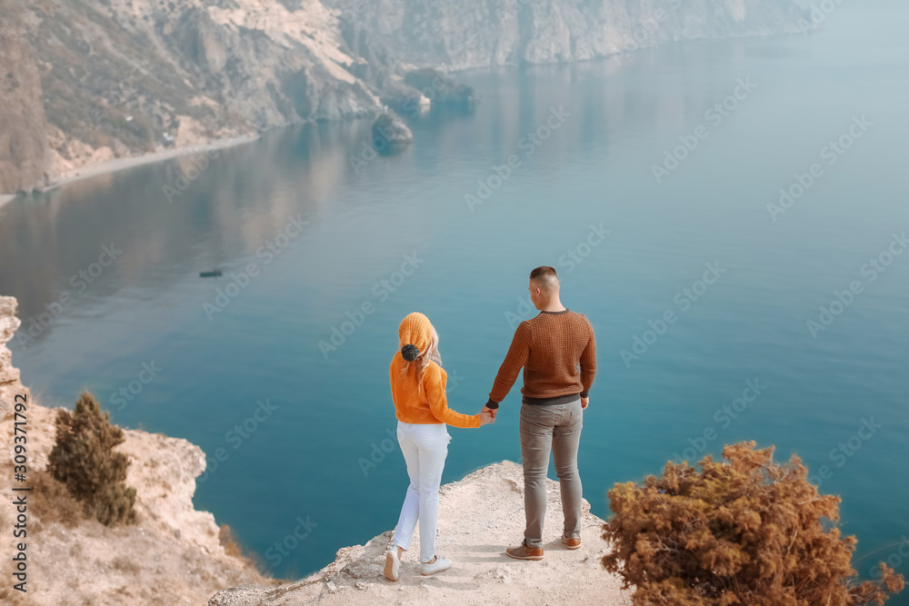 Fototapeta premium Young men and a woman stand on top of a mountain with panoramic views of the sea bay.