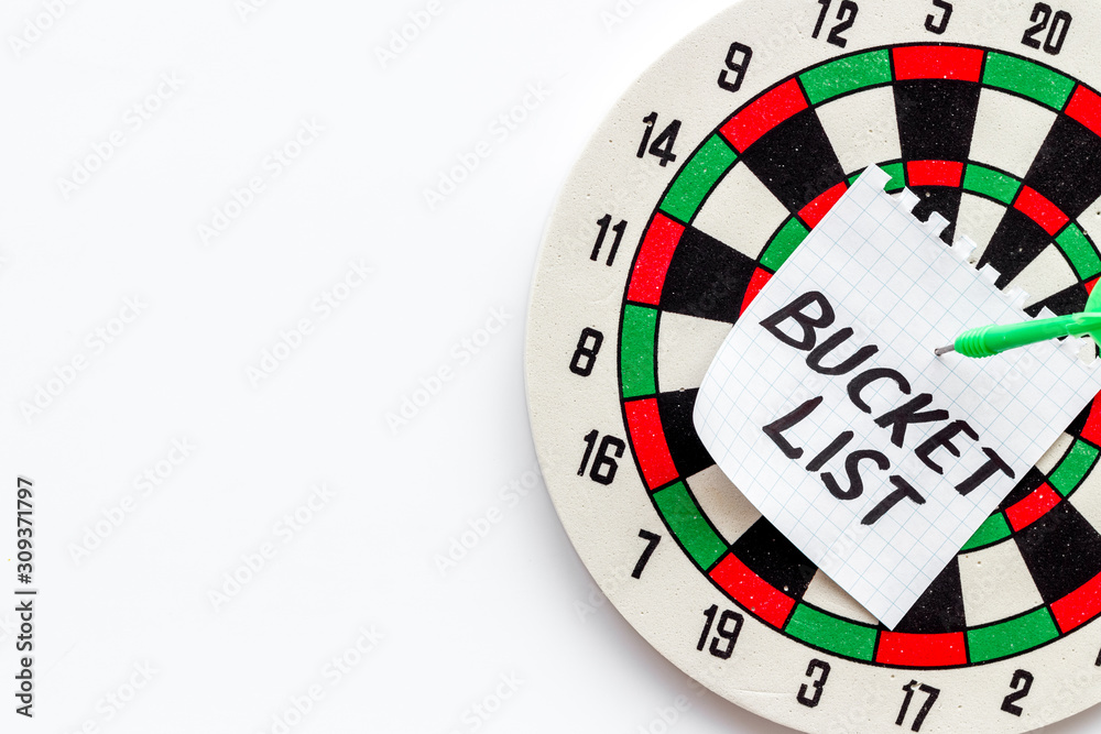 Bucket list attached by dart to dart board on white background top-down copy space Bucket list attached by dart to dart board on white background top-down copy space