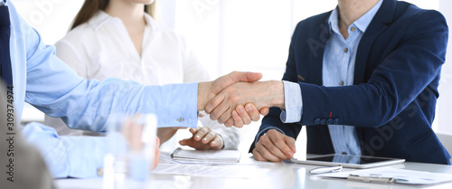 Business people shaking hands at meeting or negotiation, close-up. Group of unknown businessmen and women in modern office. Teamwork, partnership and handshake concept, toned picture