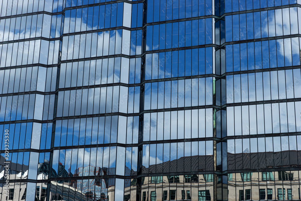 Windows of a skyscraper with reflection of blue sky and white clouds. Glass facade of a modern office building