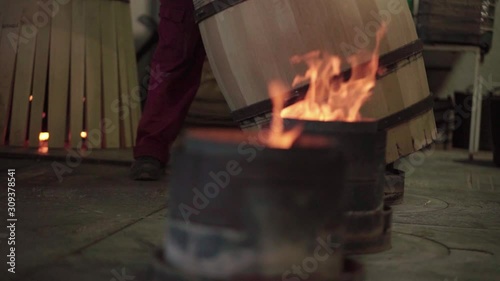 Barrel maker placing wooden barrel over burner for charring, slow motion medium shot photo