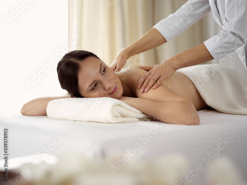 Pretty brunette woman enjoying procedure of back massage in spa salon. Beauty concept