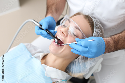 Dentist drilling teeth of young womans laying in chair. Selective focus