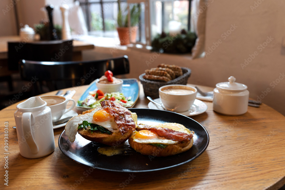English breakfast with toast with fried egg and bacon on a plate in restaurant. Tasty food for lunch with cup of coffee. Closeup. English breakfast with toast with fried egg and bacon on a plate in restaurant. Tasty food for lunch with cup of coffee. Closeup.