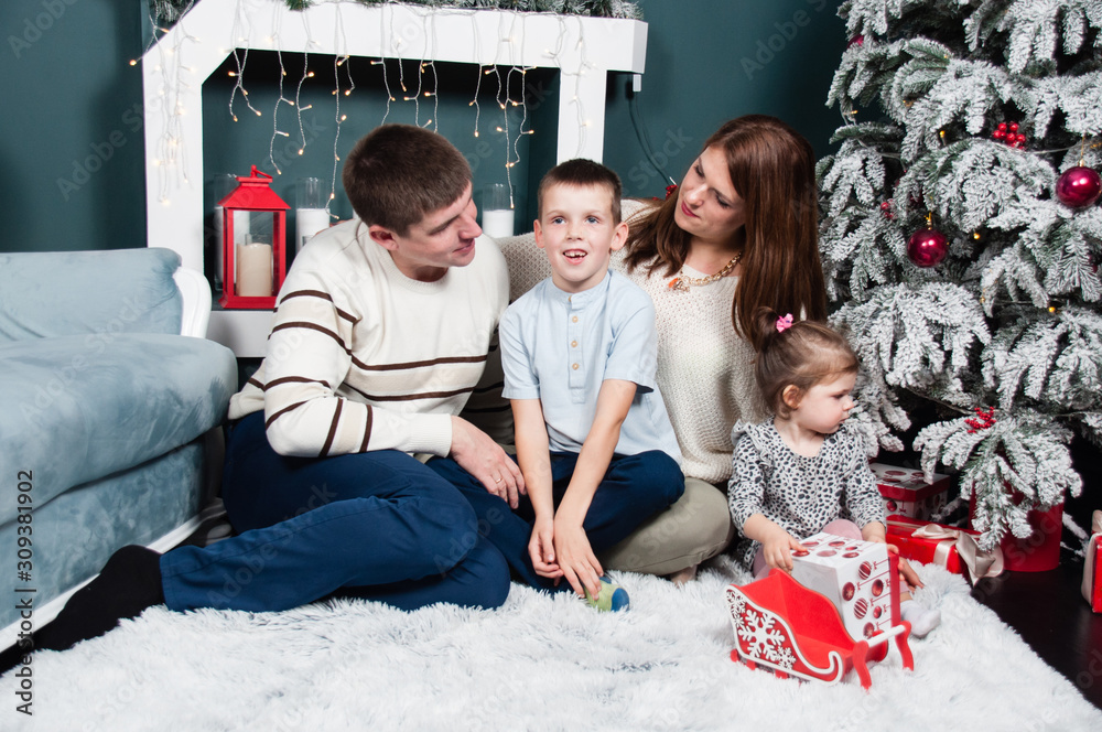 Family, parents and two children, boy and girl, smiling, having fun near the fireplace of a Christmas tree on the carpet