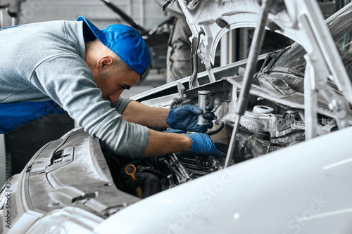 Mechanic in blue overalls checking serviceability of car engine © serhiibobyk