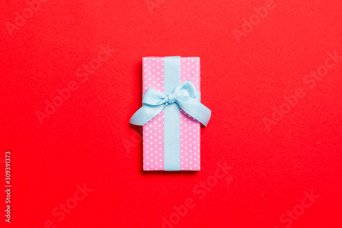 wrapped Christmas or other holiday handmade present in paper with blue ribbon on red background. Present box, decoration of gift on colored table, top view with copy space