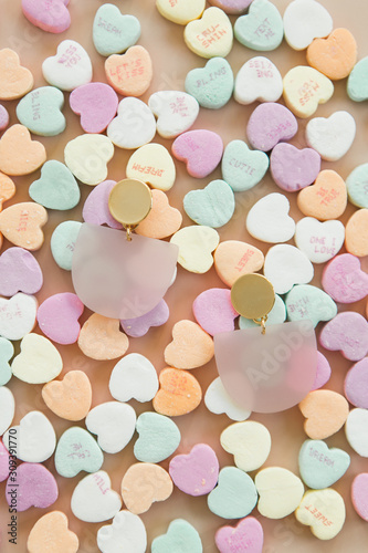 Modern valentines day jewelry on pink background with conversation heart candy