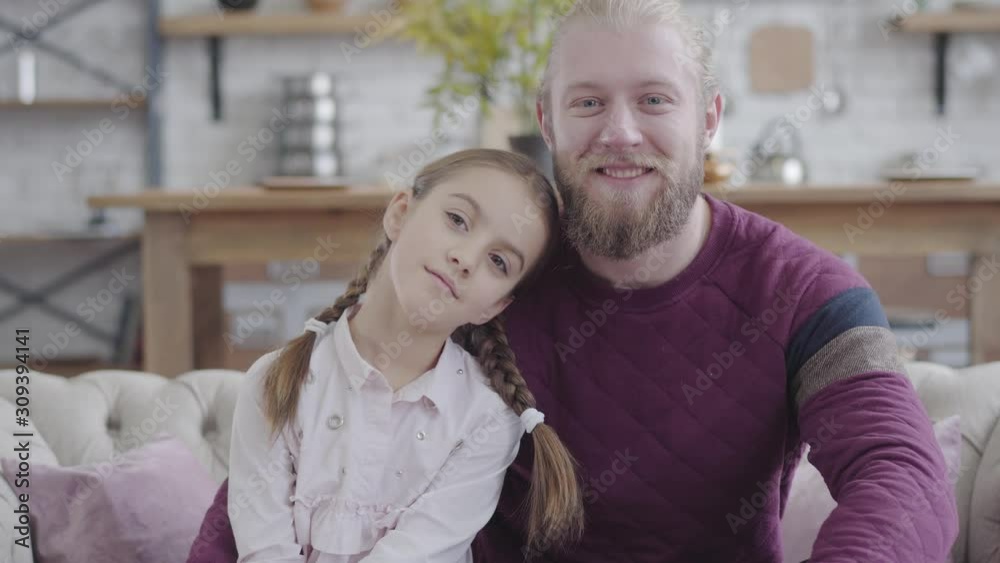 Portrait of happy Caucasian daughter putting head on father's shoulder, looking at camera and smiling. Young bearded man and teenage girl with braided pigtails posing at home. Parenthood, happiness Portrait of happy Caucasian daughter putting head on father's shoulder, looking at camera and smiling. Young bearded man and teenage girl with braided pigtails posing at home. Parenthood, happiness