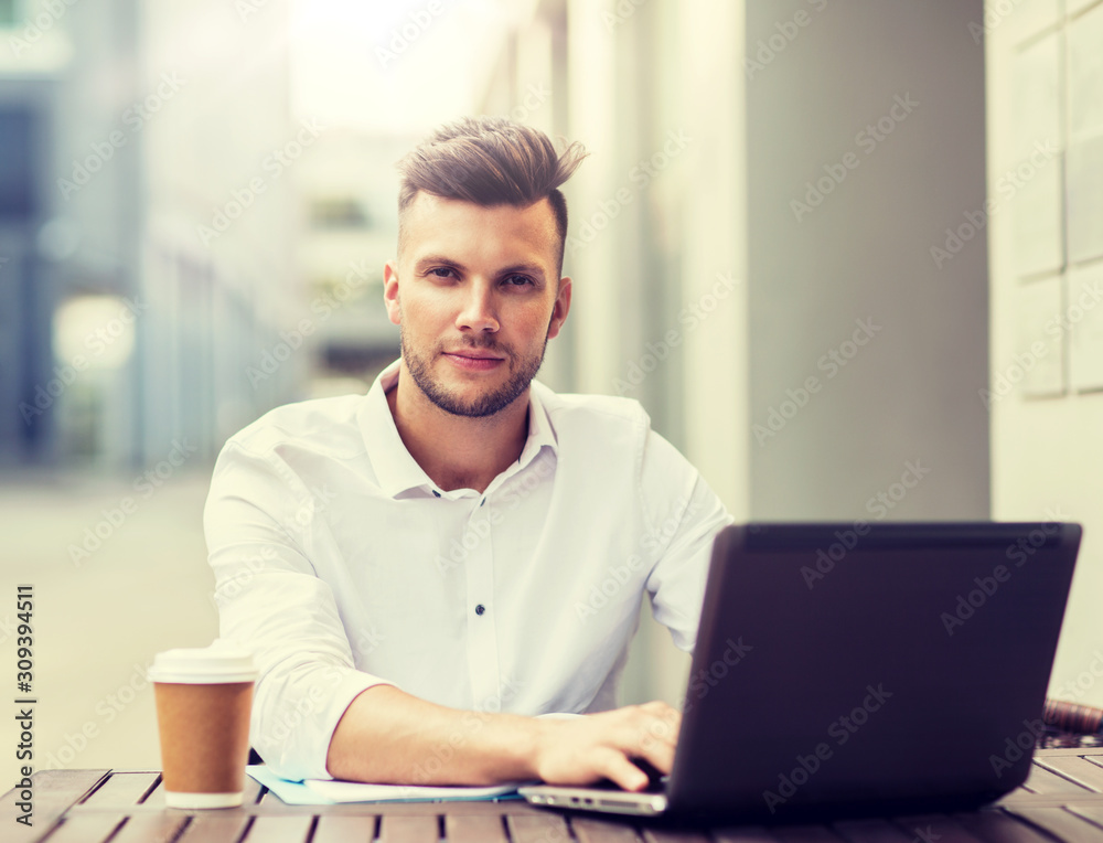 business, technology and people concept - young man with laptop computer and coffee cup at city street cafe