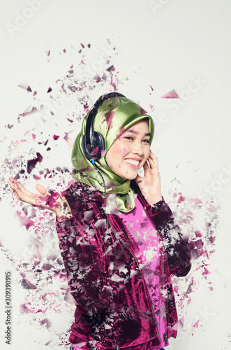 Studio shot, portrait of young beautiful Asian muslim wearing hijab listening to music with headset