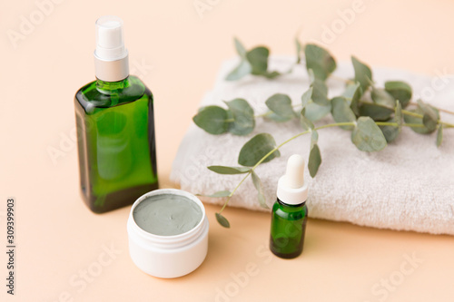 beauty, spa and wellness concept - serum, clay mask, oil and eucalyptus cinerea on bath towel