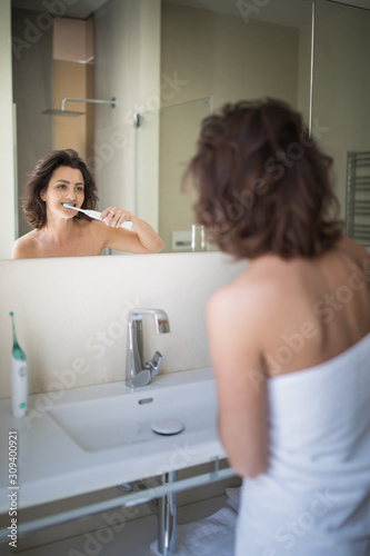 Pretty, middle aged woman brushing her teeth in a modern design bathroom
