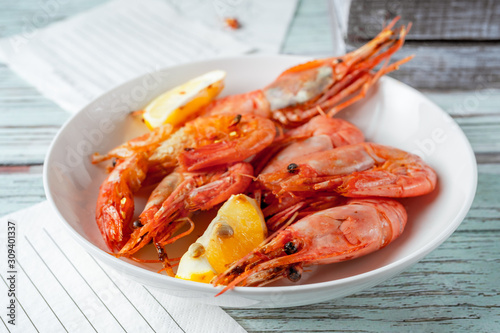 Jumbo prawns with lemon wedges served on white plate, paper napkins on wooden background, closeup view