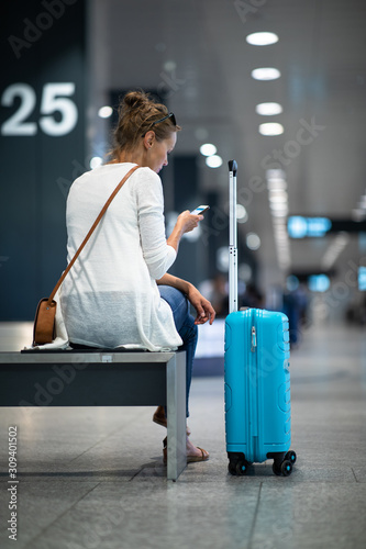 Young woman with her luggage at an international airport, waiting for her luggage to arrive at the baggage claim zone photo