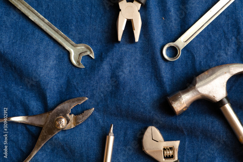 Hand tools such as hammers, pliers, wrenches of various types and screwdrivers that are arranged in a loop on the blue denim background.