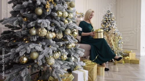 A young woman holds a gift near the Christmas tree. The girl smiles sitting with a gift for Christmas. Christmas tree upside down.