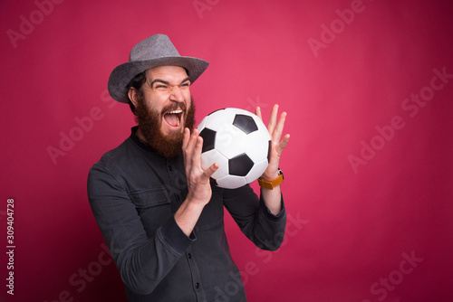 Fototapeta Naklejka Na Ścianę i Meble -  Amazed bearded man holding soccer ball and screaming