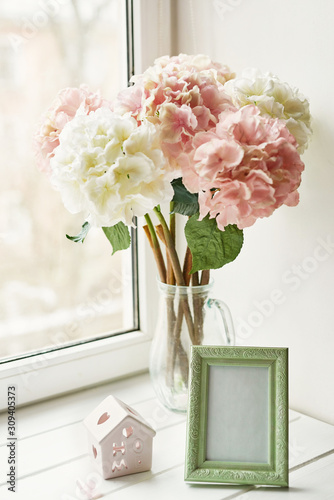 Light pink hydrangea for wedding bouquet in glass vase and photo frame on window background. Mother's day or March 8 greeting card template. Spring card concept. Beautiful bouquet of flowers in vase