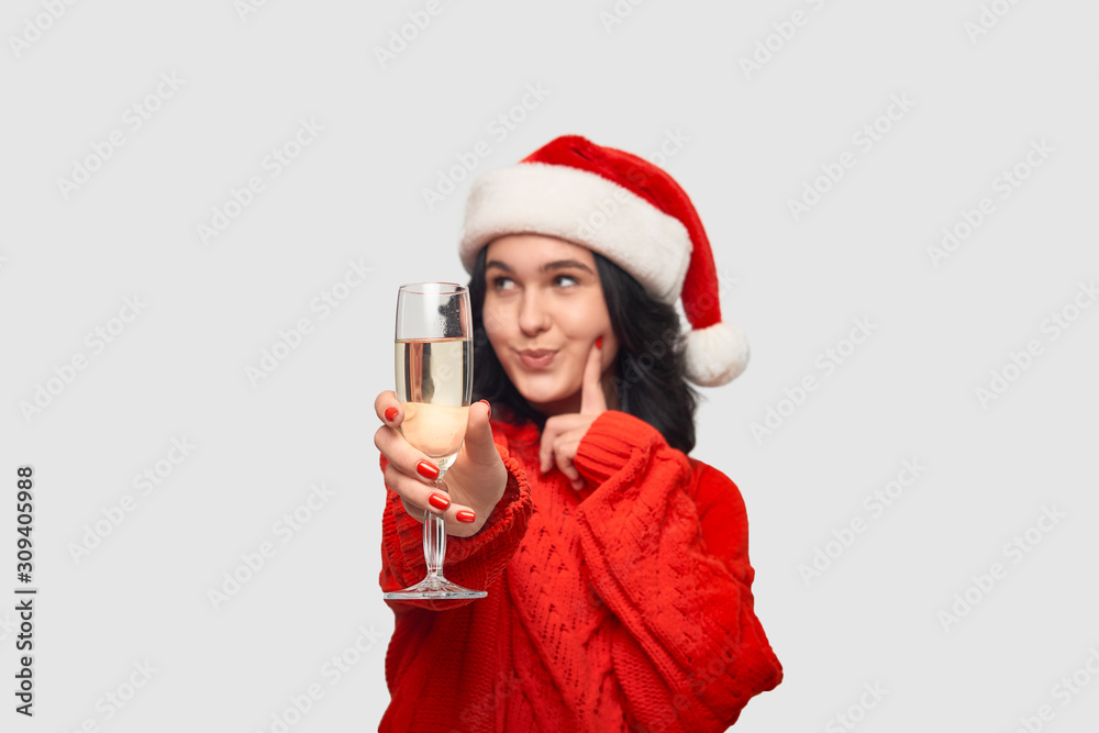Beautiful brunette girl in a red sweater and Santa hat holding glass of champagne. Beautiful brunette girl in a red sweater and Santa hat holding glass of champagne.