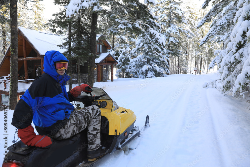 Man riding snomobile in the mountains near cabin houses and trees.