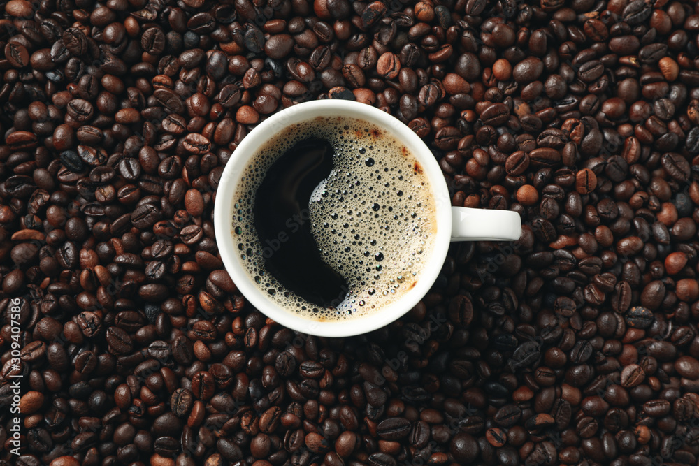 Cup of coffee on coffee beans background, top view