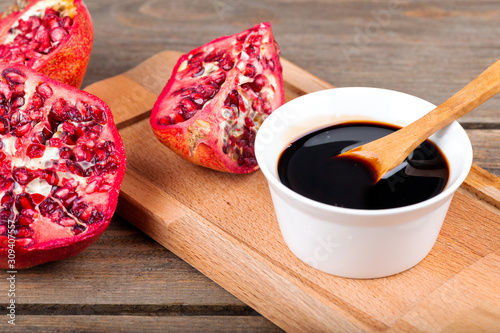 Homemade pomegranate sauce in a bowl with a spoon, fresh open pomegranate on a wooden background