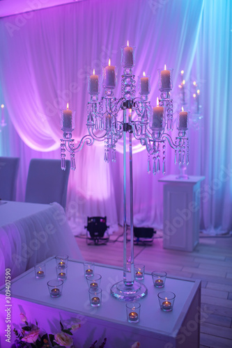 Festive table decorated with composition of candles and silver candlesticks in colored light in the banquet hall. Table newlyweds in the banquet area on wedding party.