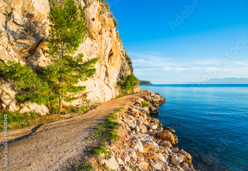Walking path along the sea coast with blue water at sunset in Greece