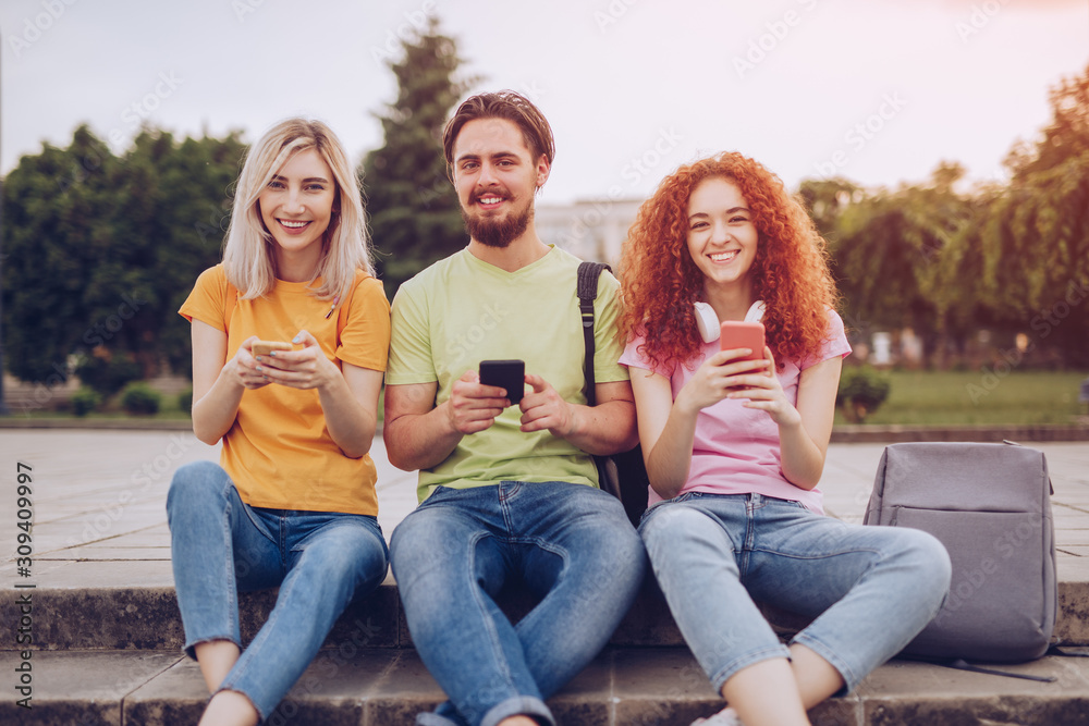 Cheerful students using smartphones in park