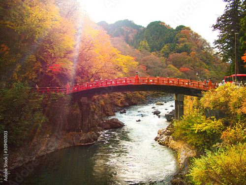 Red bridge over flowing river stream with autumn leaves and sunlight