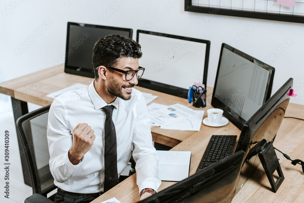 high angle view of smiling bi-racial trader showing yes gesture and looking at computer high angle view of smiling bi-racial trader showing yes gesture and looking at computer
