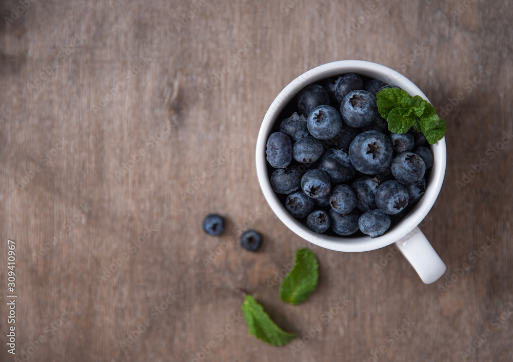 Fresh and sweet blueberry in cup with mint on brown wood background Fresh and sweet blueberry in cup with mint on brown wood background