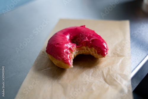 One Pink Glazed Vegan Donut with a Bite Taken Out of it photo