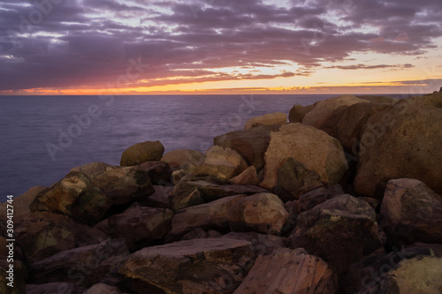 Purtple sunset in Puerto Rico Gran Canaria with rocks up front, orange sun and smooth calm water © Marcin