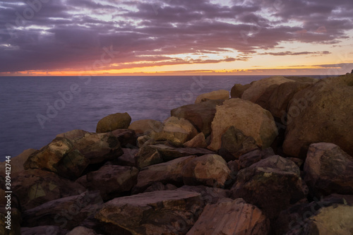 Purtple sunset in Puerto Rico Gran Canaria with rocks up front, orange sun and smooth calm water photo