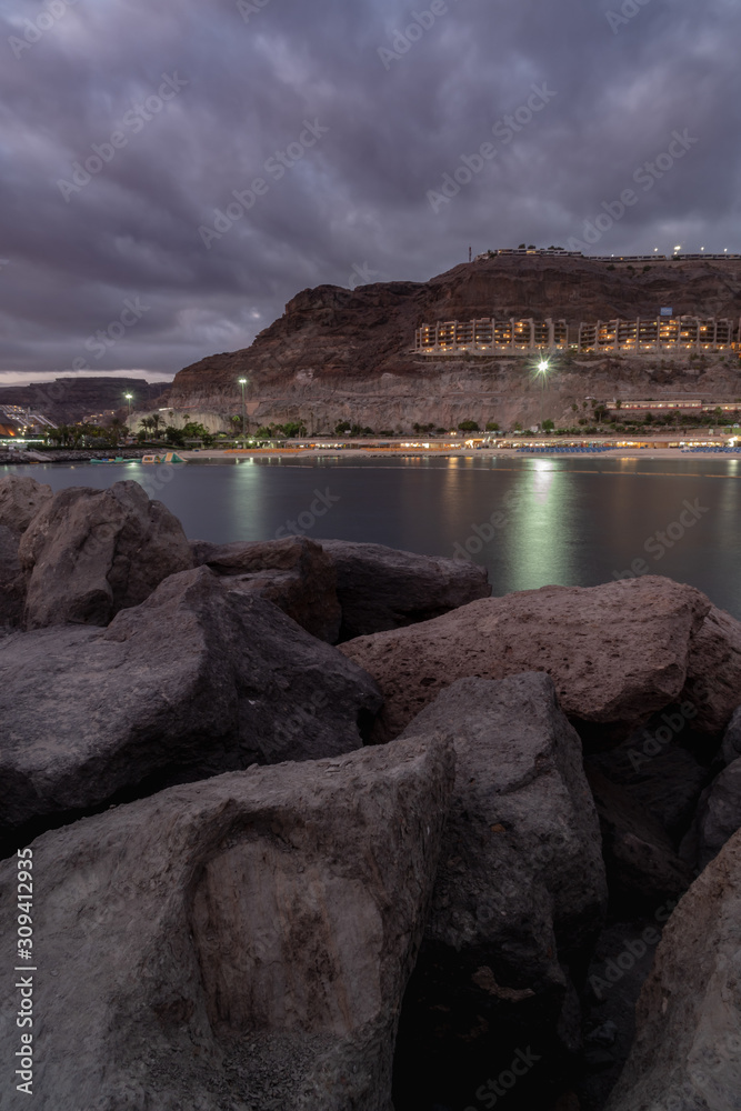 Panoramic view on the bay at night in Puerto Rico, Gran Canaria, Spain. Iluminated buildings in background and silky water with pedalo floating