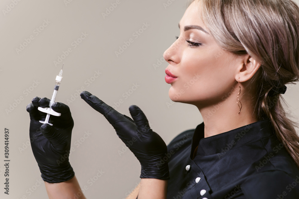 Obraz premium Portrait of doctor in cosmetological clinic. Beautician holds the syringe like a gun and blows it off. Filler for facial contouring or lips injection. Healthcare. Hyaluronic acid, scincare concept