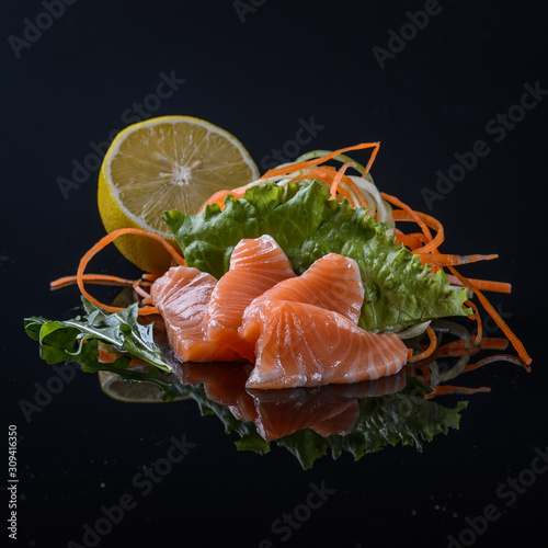 salmon's sashimi with salad and lemon on black background