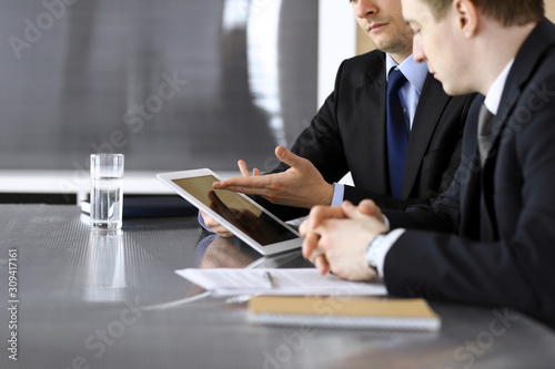 Businessman using tablet computer and work together with his colleague or partner at the glass desk in modern office, close-up. Unknown business people at meeting