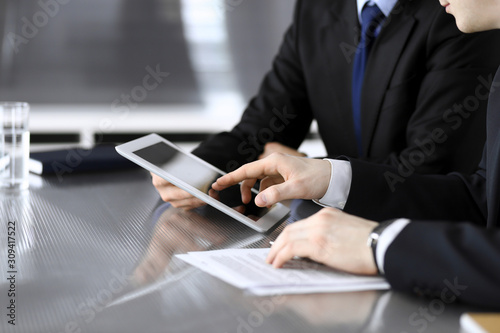 Businessman using tablet computer and work together with his colleague or partner at the glass desk in modern office, close-up. Unknown business people at meeting