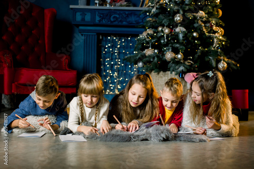 a group of young children lie on a warm woolen blanket on the background of a Christmas tree and write a letter to Santa