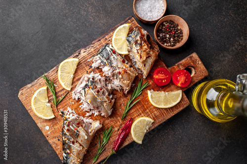 baked mackerel on a cutting board with lemon and spices on a stone background, ready to eat