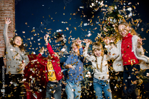 Charming and beautiful little children playing with confetti during a holiday on the background of a Christmas decorations. Winter and New Year concept.