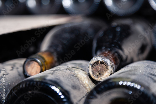 Closeup dark dusty wine bottles with old crumbly cork. Long aging, musty winery vault, rare ancient collection, cork worm
