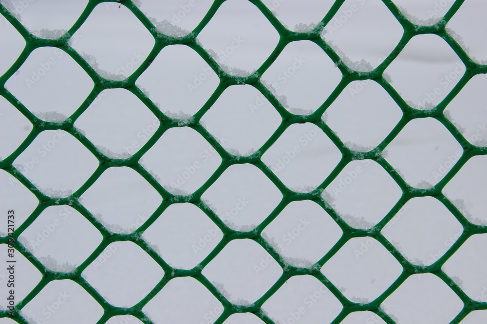 Snowflakes in cells of the green mesh fence Snowflakes in cells of the green mesh fence
