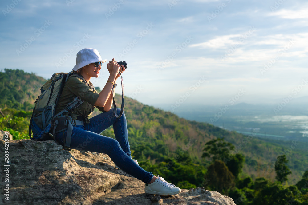 Asian woman traveler with backpack holding camera and looking at amazing mountains and forest, travel holiday relaxation concept.
